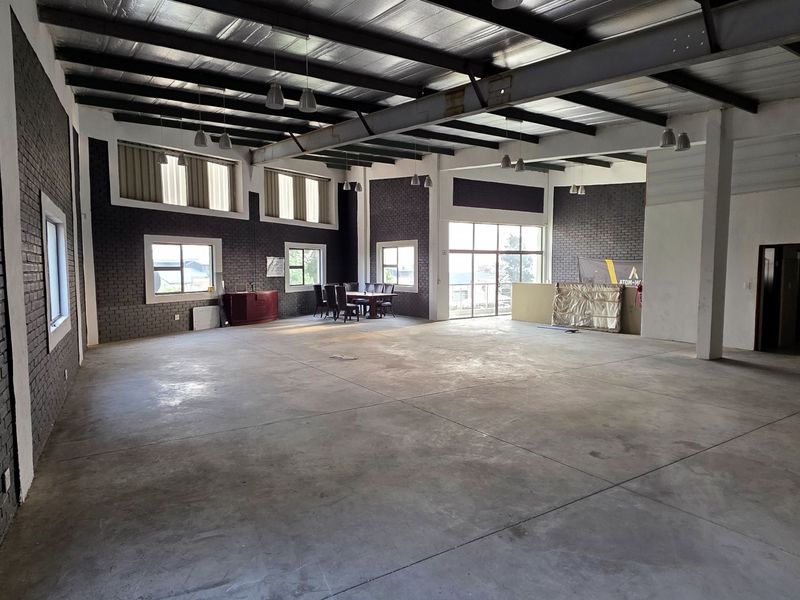Spacious open-plan industrial unit featuring exposed steel roof trusses, polished concrete flooring, and dark brick feature walls with ample natural light.