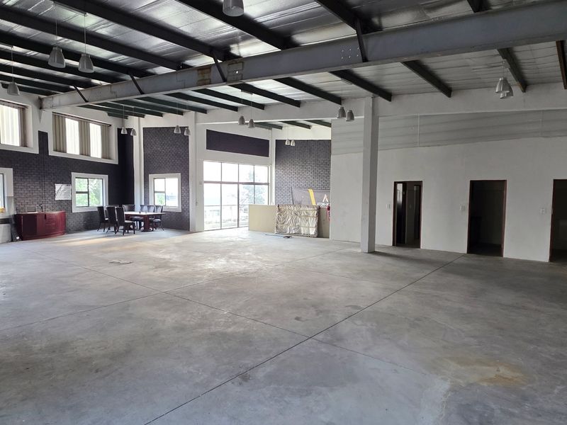 Spacious open-plan industrial unit featuring high ceilings with exposed steel trusses, polished concrete flooring, and large windows providing ample natural light.