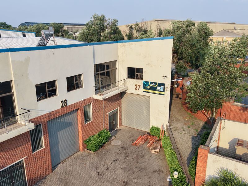 Aerial view of an industrial property featuring brick facade, roller shutter doors, paved driveway, and perimeter security fencing.