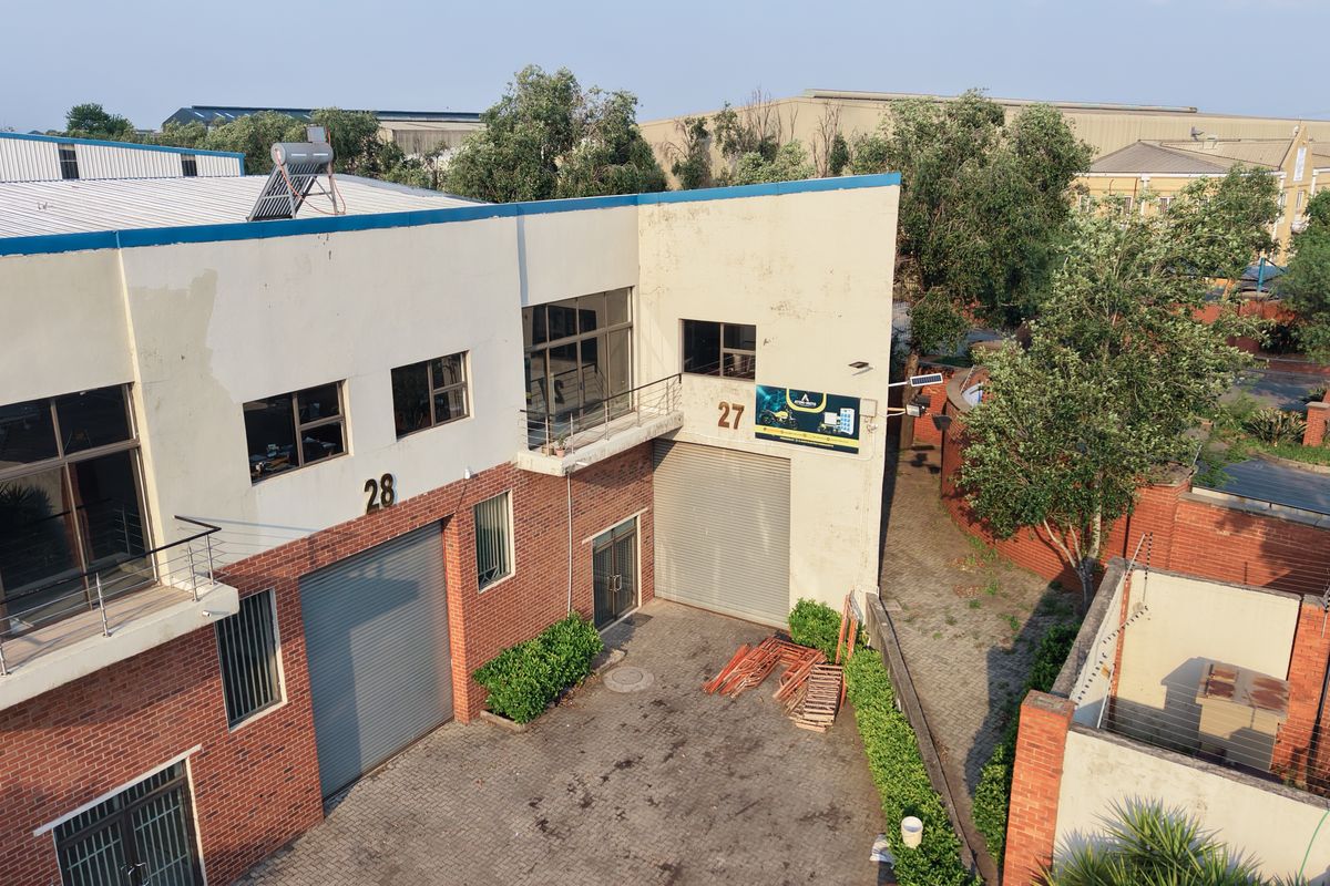 Aerial view of an industrial property featuring brick facade, roller shutter doors, paved driveway, and perimeter security fencing.