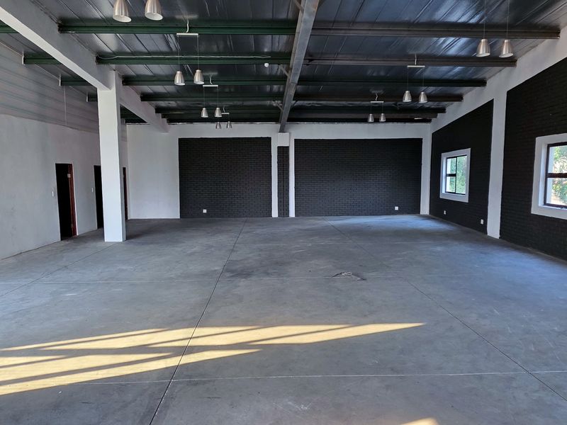 Spacious industrial open-plan area featuring polished concrete floors, exposed steel beams, and modern brick feature walls, ideal for versatile commercial or creative use.