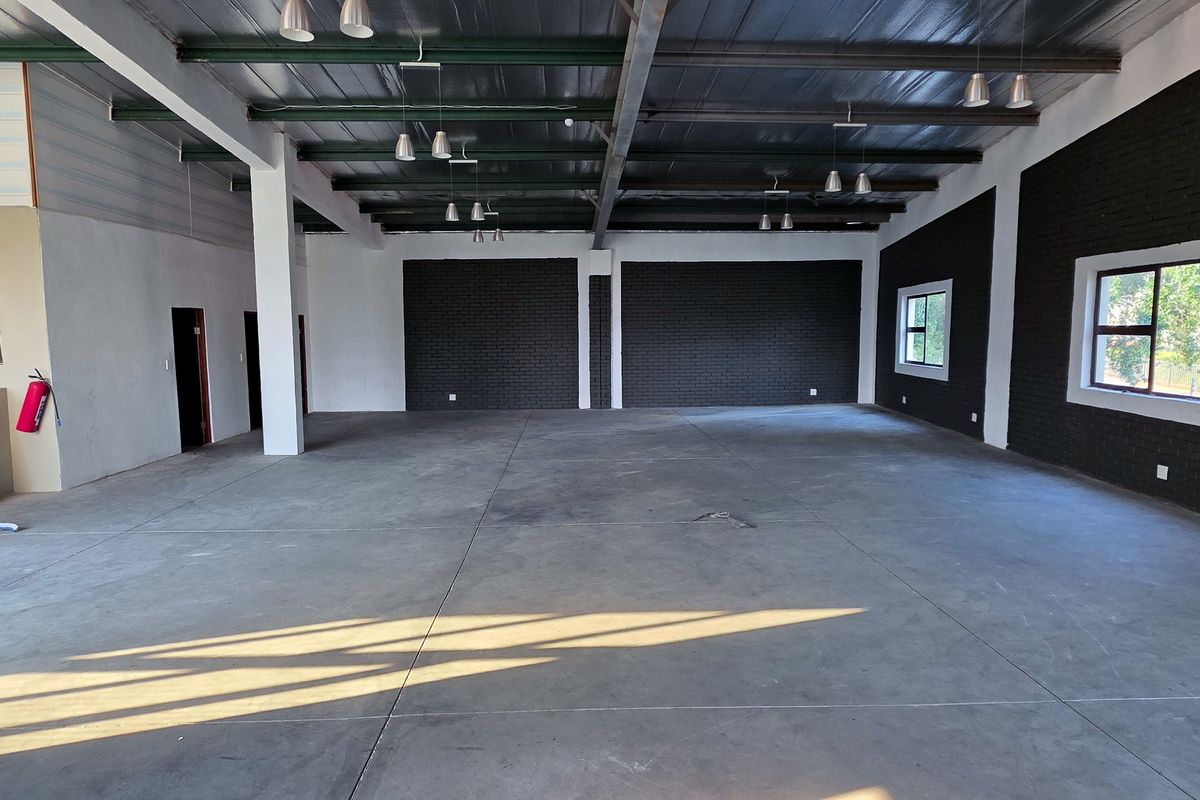 Spacious industrial open-plan area featuring polished concrete floors, exposed steel beams, and modern brick feature walls, ideal for versatile commercial or creative use.
