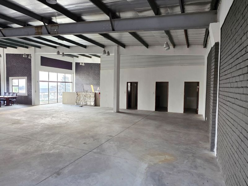 Spacious open-plan industrial unit featuring exposed steel beams, concrete flooring, and brick wall accents, offering a versatile layout suitable for various commercial uses.