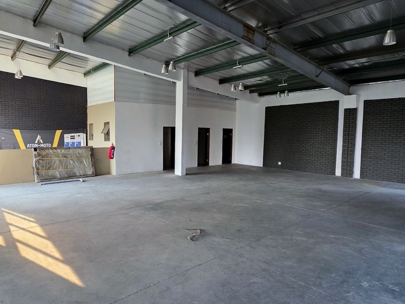 Spacious industrial open-plan unit featuring polished concrete floors, exposed steel roof trusses, and modern dark brick feature walls, ideal for versatile commercial use.