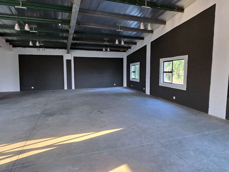 Spacious open-plan industrial unit featuring polished concrete floors, exposed steel roof structure, and modern dark-painted brick feature walls with ample natural light.
