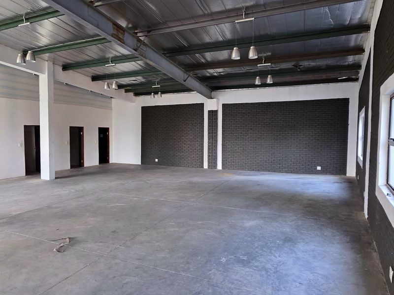 Spacious industrial open-plan area featuring exposed steel roof trusses, polished concrete flooring, and modern dark-painted brick feature walls with ample natural light.