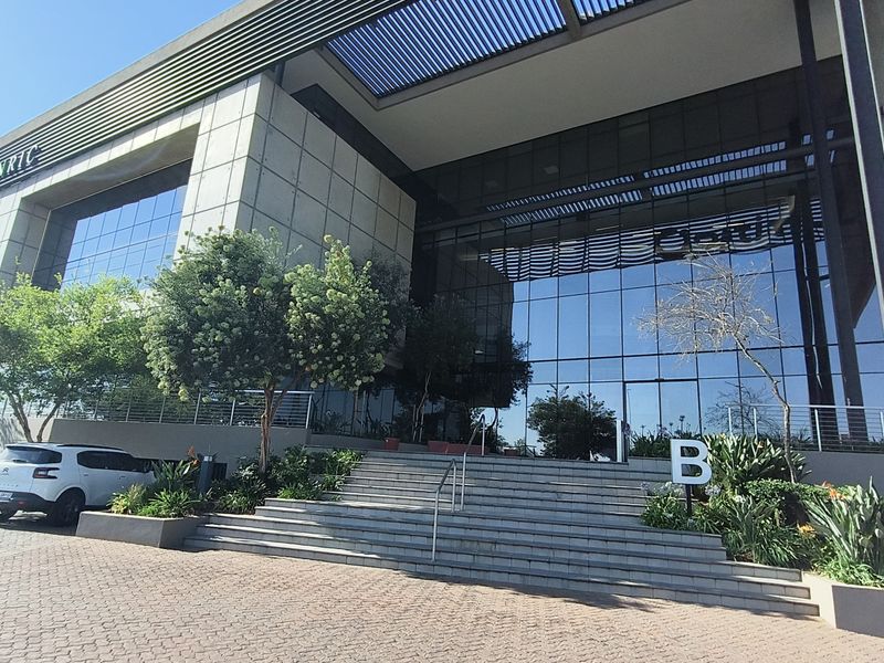 Modern office building entrance featuring a glass facade, stone cladding, and a wide concrete staircase leading to the main entry.