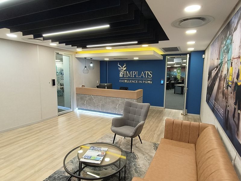 Modern office reception area featuring a branded front desk, contemporary baffle ceiling, recessed lighting, and high-quality laminate flooring with glass partition access.