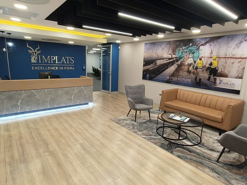 Modern office reception area featuring a professional reception desk, wood-look laminate flooring, and contemporary baffle ceiling design with integrated lighting.