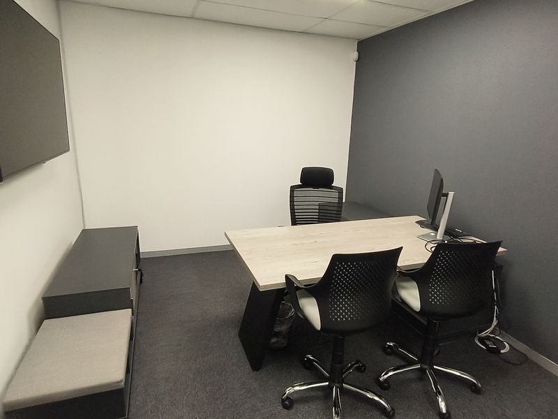 A functional office space featuring carpeted flooring, a suspended ceiling, and a dark grey accent wall, providing a professional work environment.