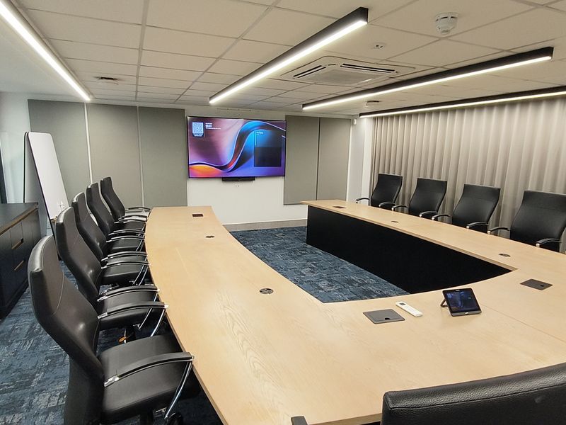 A modern, well-maintained boardroom featuring a large U-shaped conference table, integrated AV equipment, acoustic wall paneling, and professional linear lighting.