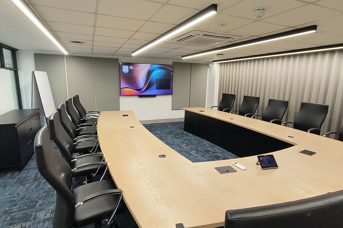 A modern, well-maintained boardroom featuring a large U-shaped conference table, integrated AV equipment, acoustic wall paneling, and professional linear lighting.