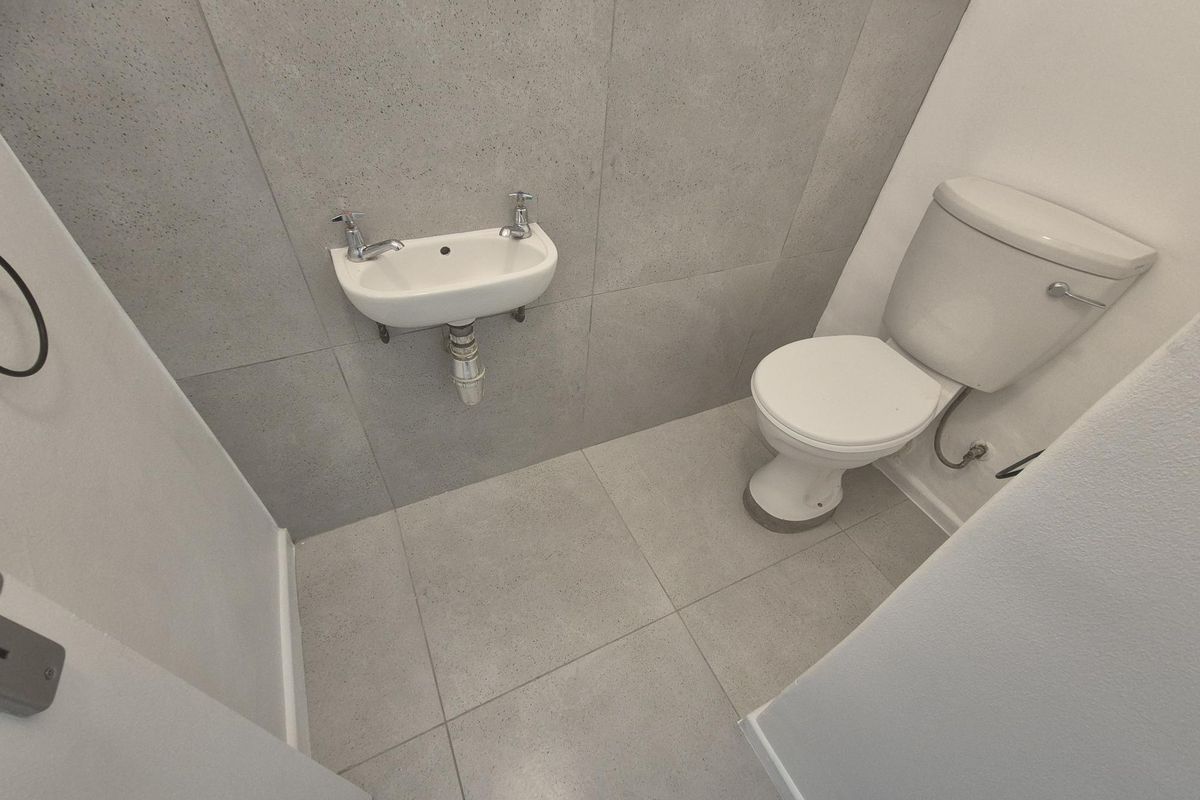 A compact guest bathroom featuring modern grey floor-to-ceiling tiling, a wall-mounted basin, and a standard toilet.