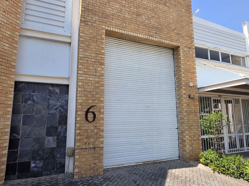 Front elevation of an industrial unit featuring a large roller shutter door, face brick exterior, and a secure pedestrian entrance with security gate.
