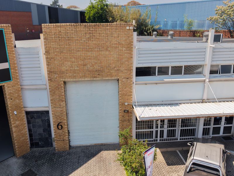 Aerial view of an industrial unit featuring a roller shutter door, brick facade, and secure entrance with paved driveway access.