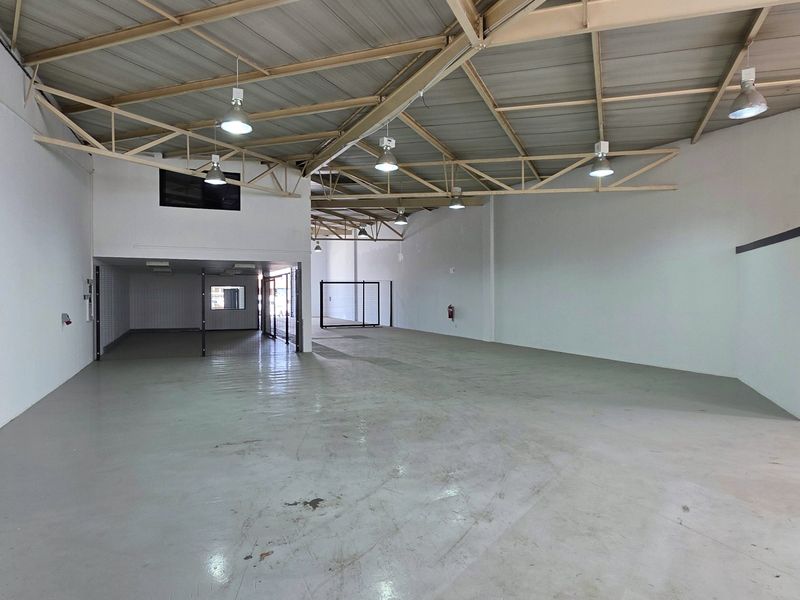 Spacious industrial warehouse unit featuring high exposed steel roof trusses, durable concrete flooring, and integrated mezzanine level, suitable for various commercial or storage applications.