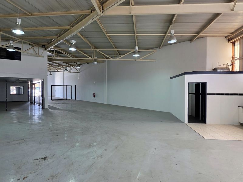 Spacious industrial open-plan warehouse featuring exposed steel roof trusses, high ceilings, polished concrete flooring, and a functional kitchenette area.