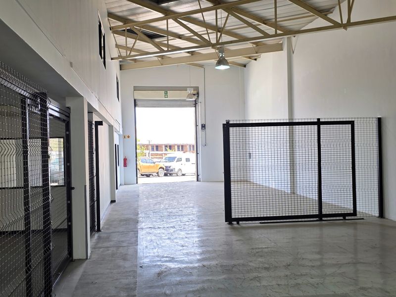 Spacious industrial warehouse unit featuring high ceilings with exposed steel trusses, concrete flooring, and secure wire mesh partitioning.