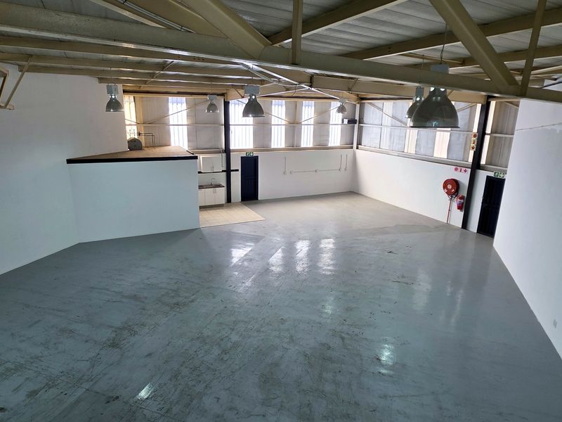 Spacious industrial warehouse unit featuring high ceilings with exposed steel trusses, durable epoxy flooring, mezzanine area, and a small kitchenette.