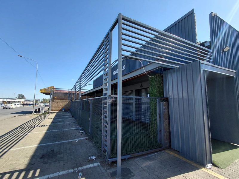 Exterior view of a commercial property featuring a metal-clad facade, steel security fencing, and an adjacent paved parking area.