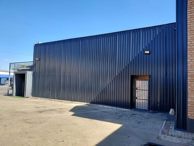 Exterior view of a commercial building featuring dark corrugated metal cladding, a secure metal door, and an adjacent paved parking area.