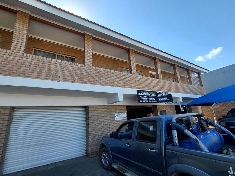 Front exterior view of a commercial brick building featuring a roller shutter garage door and an upper-level balcony with brick pillars.