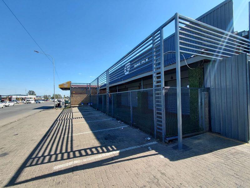 Exterior view of a commercial property featuring paved parking, metal security fencing, and a modern slatted metal facade structure.