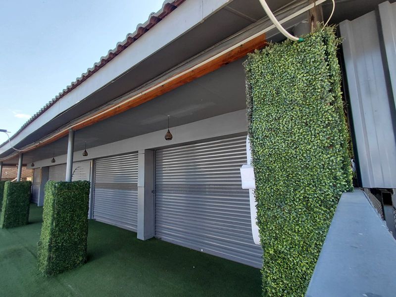 Covered outdoor patio area featuring artificial turf flooring, decorative green wall pillars, and secure metal roller shutter doors.
