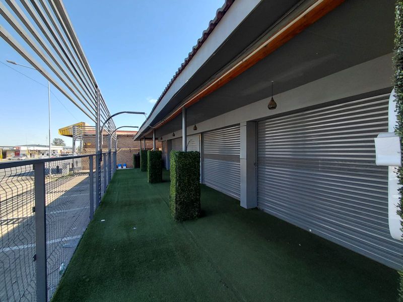 A covered outdoor patio area featuring artificial turf flooring, metal security shutters, and decorative pillars, suitable for commercial use.