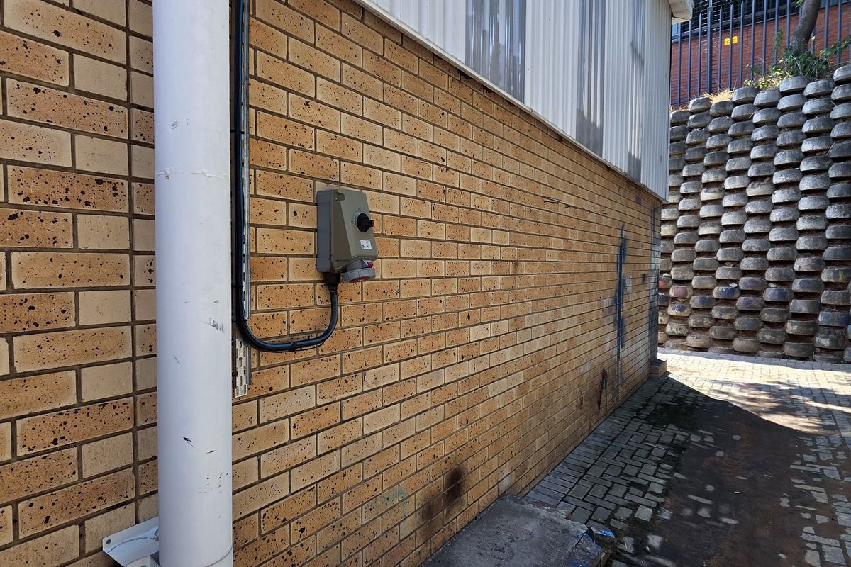 Exterior side passage featuring a brick facade, downpipe, external power point, and a concrete block retaining wall alongside a paved walkway.