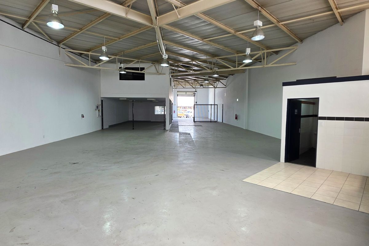 Spacious industrial warehouse unit featuring high ceilings with exposed steel trusses, concrete flooring, a mezzanine level, and a functional kitchenette area.