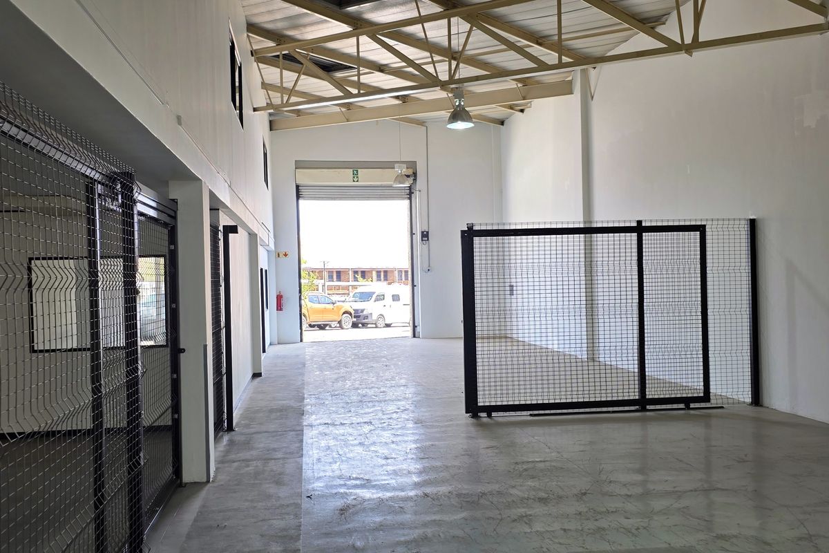 Spacious industrial warehouse unit featuring high ceilings with exposed steel trusses, concrete flooring, and secure wire mesh partitioning.