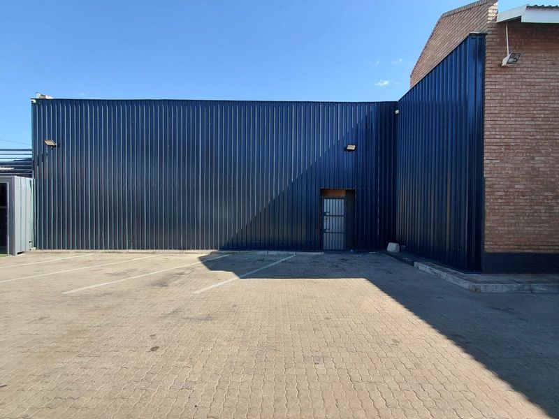 Exterior view of a commercial building featuring dark corrugated metal cladding, brickwork accents, and a paved parking area.