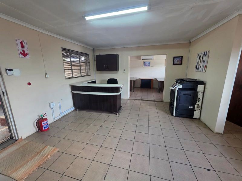 Functional office reception area featuring tiled flooring, a built-in service counter, overhead fluorescent lighting, and an adjoining workspace.