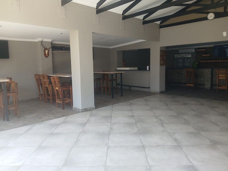 A spacious commercial bar area featuring tiled flooring, exposed ceiling beams, and a built-in bar counter, suitable for hospitality or entertainment use.