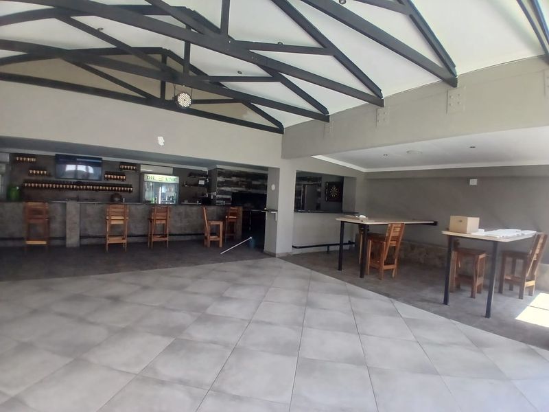 Spacious commercial bar area featuring tiled flooring, exposed roof trusses, and a built-in bar counter with integrated shelving.