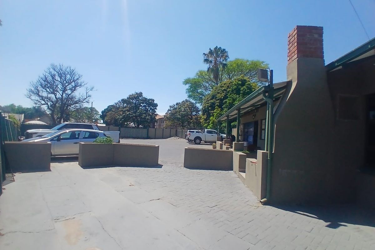 Exterior view of a commercial property featuring a paved driveway, masonry boundary walls, and a prominent brick chimney.