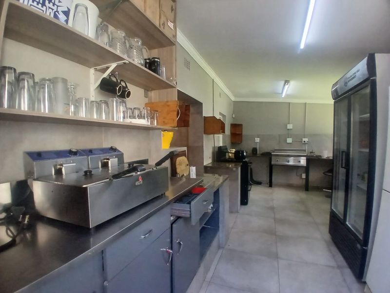 Commercial kitchen area featuring stainless steel work surfaces, built-in deep fryers, open shelving, and tiled flooring, suitable for food preparation and service.