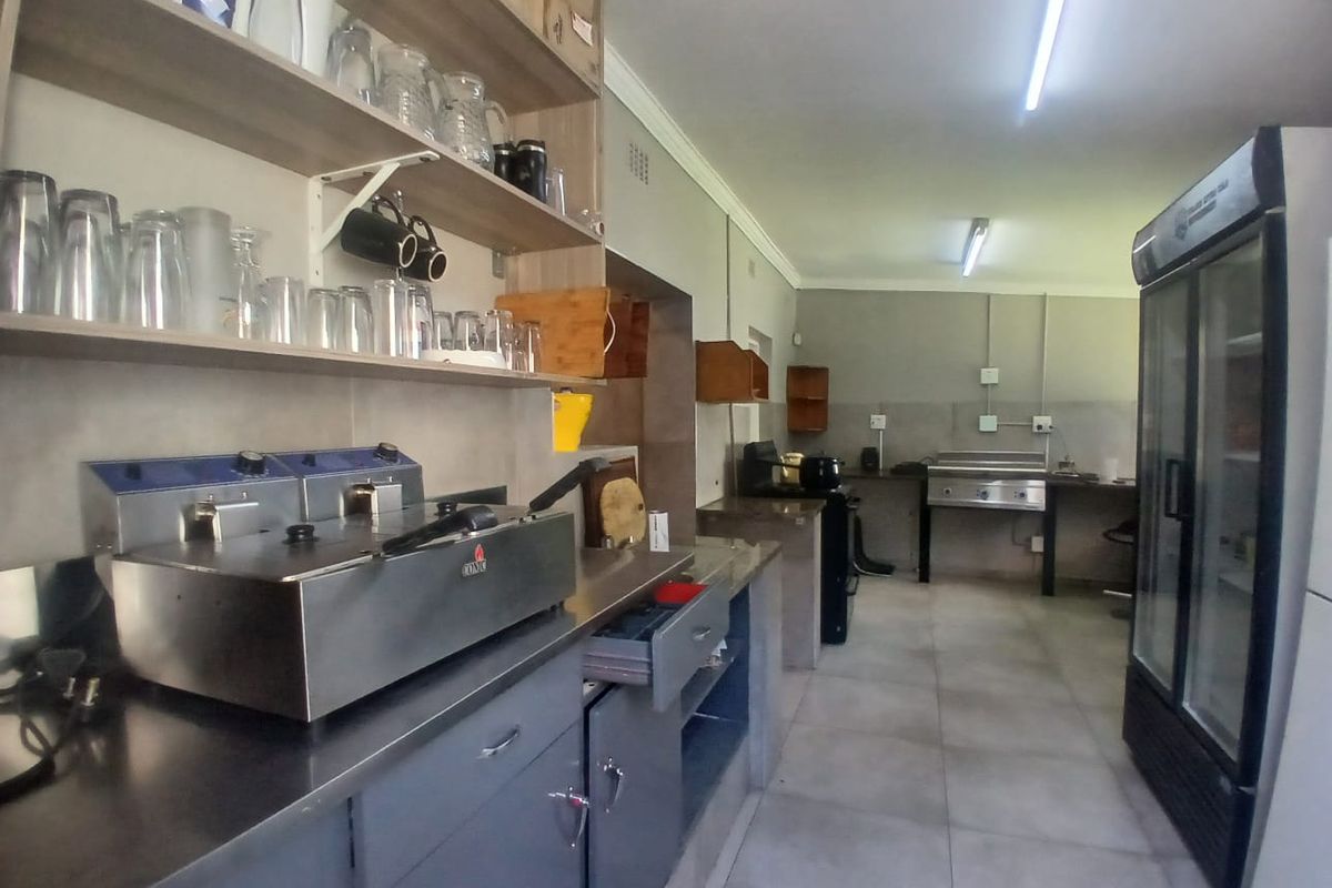 Commercial kitchen area featuring stainless steel work surfaces, built-in deep fryers, open shelving, and tiled flooring, suitable for food preparation and service.