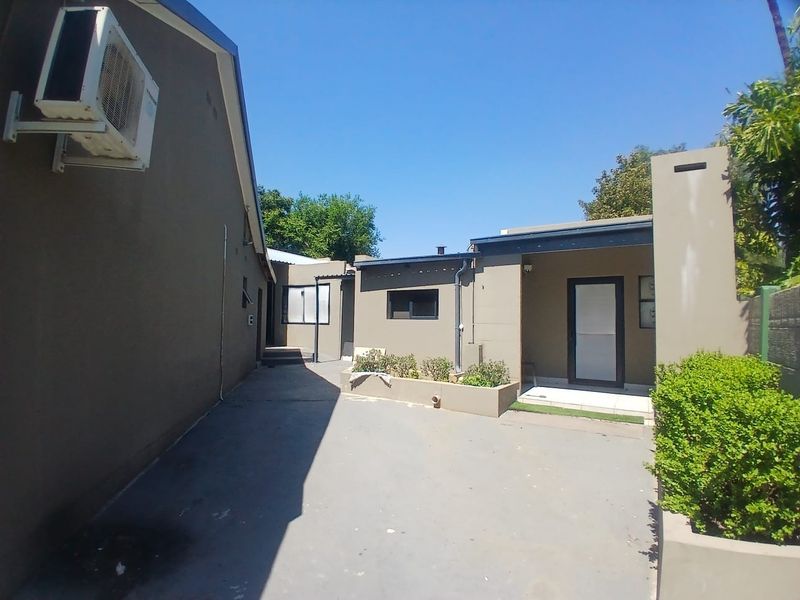 A paved rear courtyard area featuring a raised garden bed, external air conditioning unit, and access to the building structure.