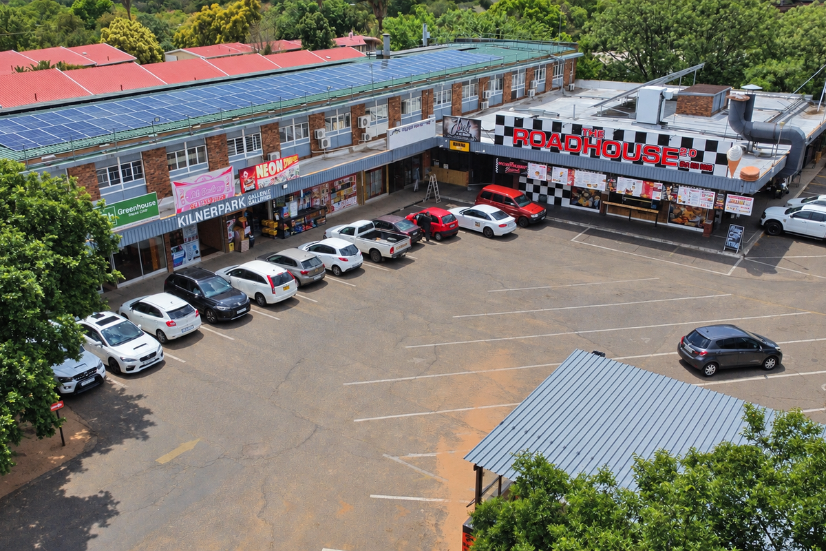 Aerial view of a retail strip center featuring a large asphalt parking area, solar panel installation, and multiple commercial storefronts.
