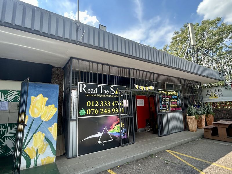 Front facade of a retail property featuring a metal security gate, signage, and a covered entrance area.