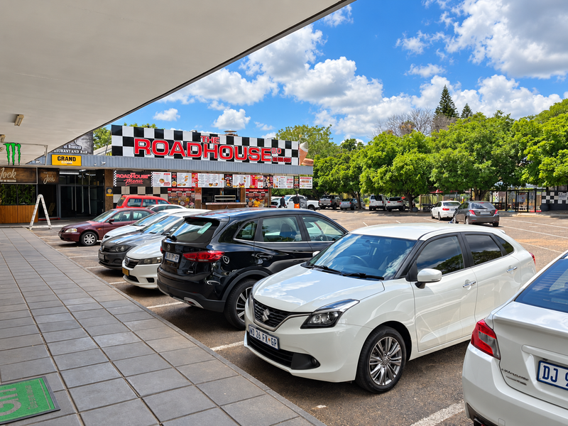 A view of a commercial retail parking area and storefront entrance with a covered walkway and signage for The Roadhouse 20.