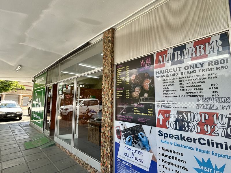 Front exterior view of a retail storefront featuring a large glass display window, covered walkway, and prominent signage for multiple businesses.
