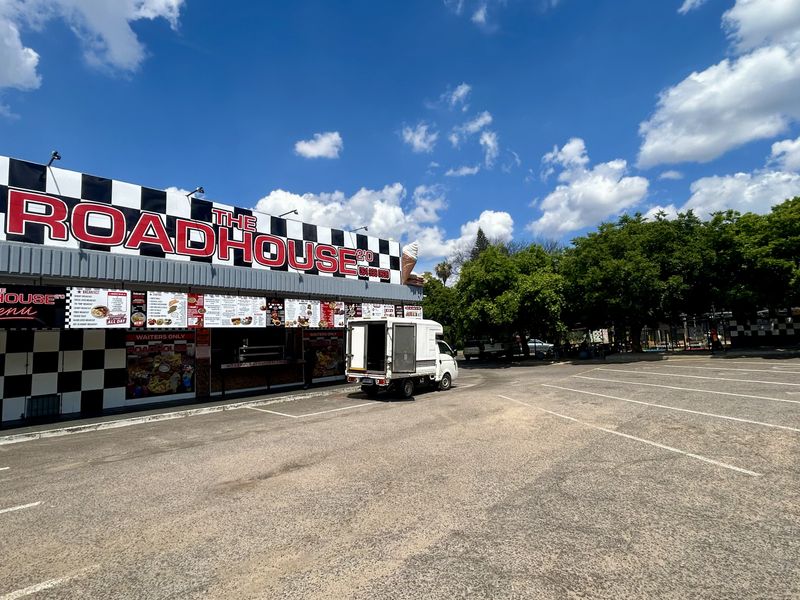 Exterior view of a retail roadhouse establishment featuring a large asphalt parking area and prominent checkered facade signage with integrated menu boards.
