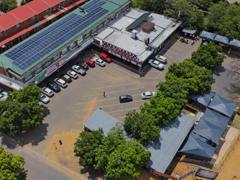 Aerial view of a commercial retail property featuring a large parking area, shaded parking bays, and a building roof equipped with solar panels.