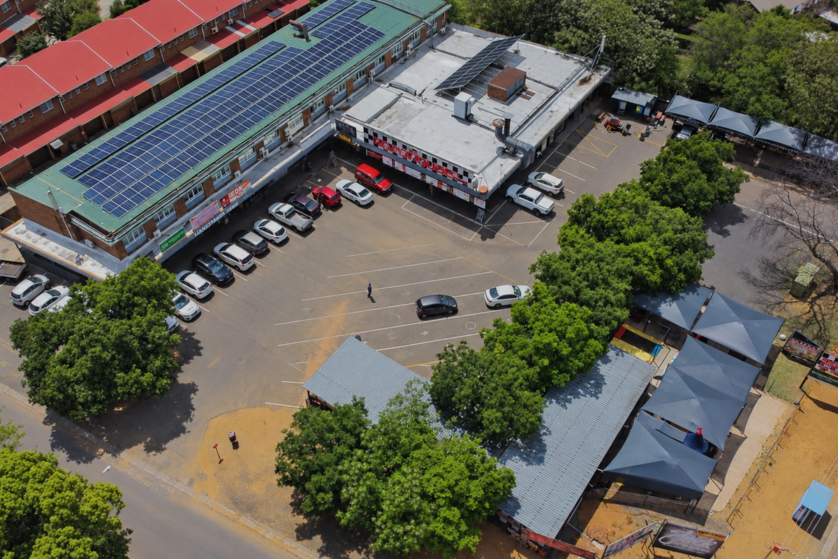 Aerial view of a commercial retail property featuring a large parking area, shaded parking bays, and a building roof equipped with solar panels.