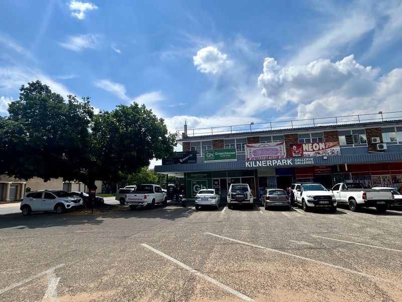 Front exterior view of Kilnerpark Galleries retail center featuring a paved parking area and multiple commercial storefronts with signage.