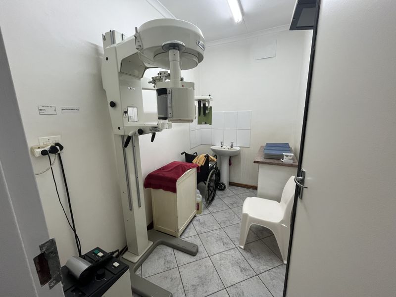 A functional medical utility room featuring a dental X-ray machine, a pedestal sink, and tiled flooring, suitable for clinical or diagnostic use.