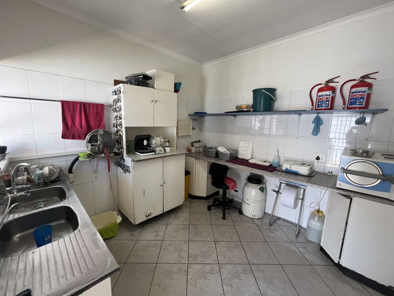 Functional utility or scullery area featuring double stainless steel sink, tiled splashbacks, built-in cabinetry, and durable ceramic floor tiles.
